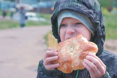Boy eating a bun on the street.の写真素材