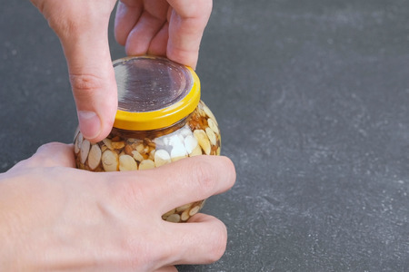 Man closes the lid of a jar of nuts in honey. Hands close-up.の写真素材