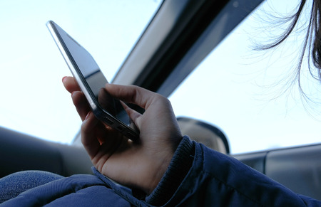 Woman in a car with a mobile phone. Closeup womans hands browsing internet pages in mobile phone.