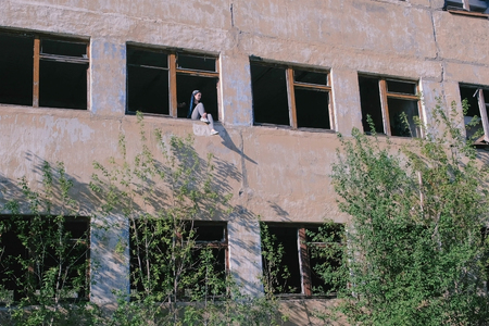 Woman sitting on window of destroyed multi-storey building with many broken windows.の写真素材