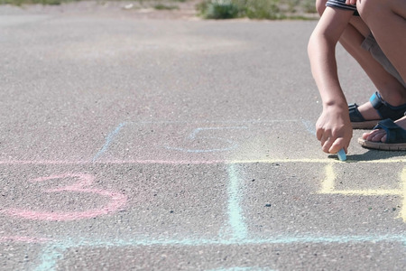 Boy is drawing hopscotch on the asphalt. Close-up hand and legs.の写真素材
