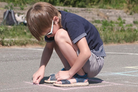 Boy is drawing hopscotch on the asphalt.の写真素材