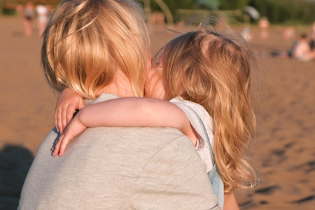 Beautiful blonde mom and daughter cuddling on the beach at sunset.の写真素材