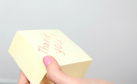 Yellow sticker paper sheet with words thank you in womans hand.の写真素材