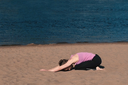Woman stretching yoga on the beach by the river in the city. Beautiful city view. Relaxing exercise.の写真素材