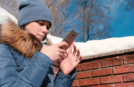 Woman is typing a message on mobile phone sitting in winter park.