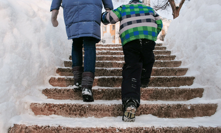 Closeup mom and sons legs rising up on a snowy ladder, staircase. Winter city park in snowy day with falling snow.の写真素材