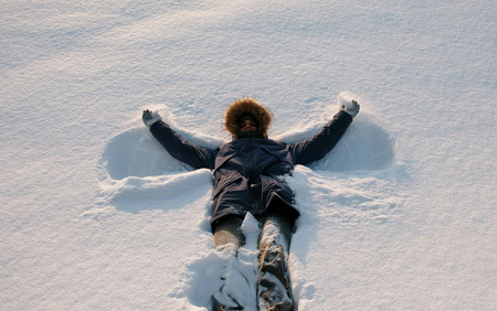 Man in blue down jacket with a fur hood makes a snow angel.の写真素材