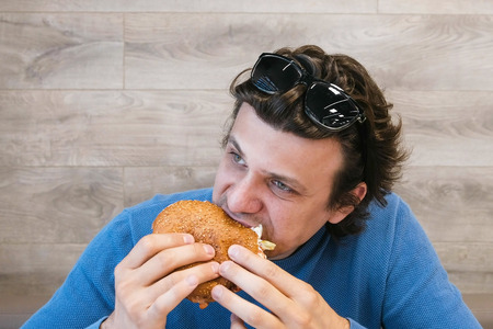 Young man eating a hamburger sitting in a cafe.