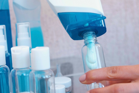 Womans hands pour blue shampoo in a small bottle of big. Travel set of jars. Bottle close-up.の写真素材