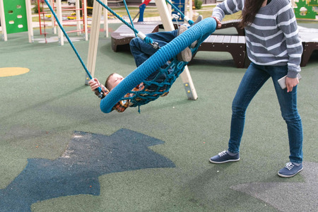 Mom swing son on empty webbed swing.