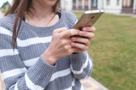 Unrecognizable brunette woman is reading something on mobile phone walking near the home.