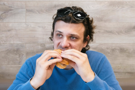 Man is eating a hotdog in cafe.