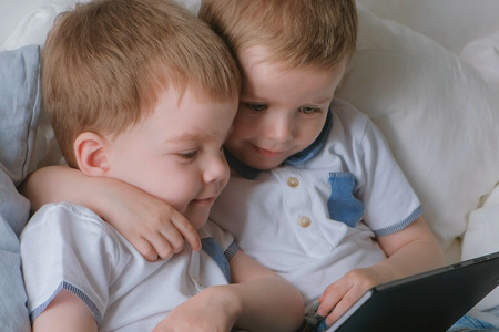 Kids with tablet. Two boys twins toddlers looking cartoon at tablet lying on the bed.の写真素材