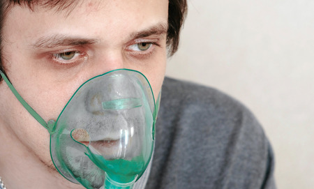 Use nebulizer and inhaler for the treatment. Closeup young mans face inhaling through inhaler mask....