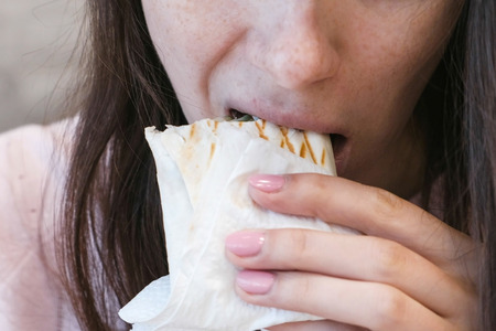 Unrecognizable young brunette woman eating danar or Shawarma sitting in a cafe.の写真素材