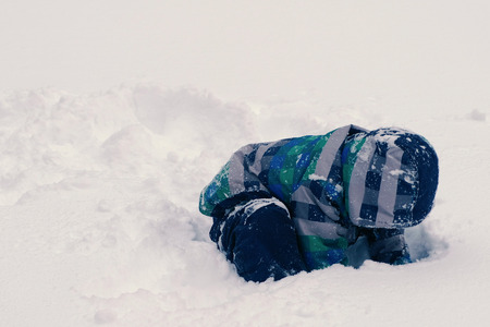 Boy digs a hole in the snow. Sits in snowdrifts.