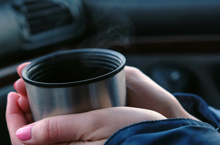 Close-up of a cup of hot tea from a flask in the hands of a woman in the car in winter.の写真素材