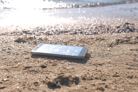 Mobile phone on the sandy sea beach with waves.の写真素材