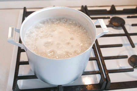 Rice is cooked in an aluminum sauce pan on a gas stove.