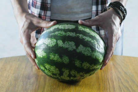 Man puts a watermelon on the kitchen table. Close-up hands.