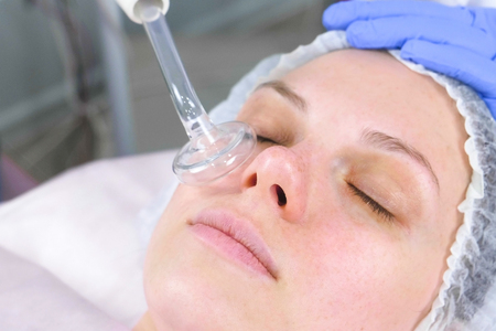 Beauty treatment facial electric darsonval therapy at cosmetology clinic.