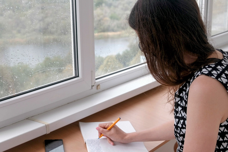 Woman is writing something in notebook sitiing on the balcony at home.の写真素材