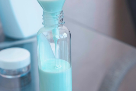 Pour blue liquid through a funnel. Travel set of jars. Bottle close-up.