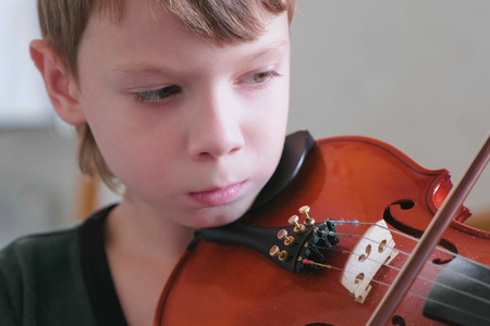 Boy of 8 years is playing violin using notes. Face cloe-up.の写真素材