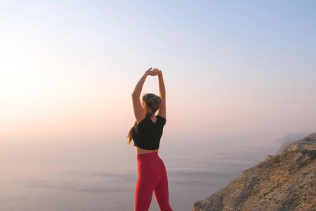 Beautiful view of woman doing yoga stretching on the mountain with sea view at sunsetの写真素材