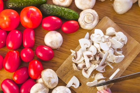 Woman's hands is cutting mushrooms champignons on the wooden bord on kitchen tableの写真素材
