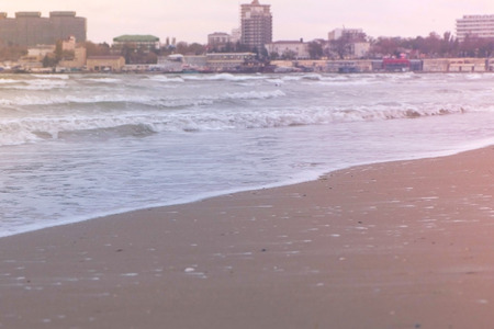 Stormy waves in the sea. Beautiful seascape, sandy beach and coastal town on background at pink...