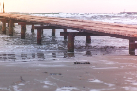 Rusty wooden pier on the beach. Storm waves in the sea, beautiful seascape at sunset.の写真素材