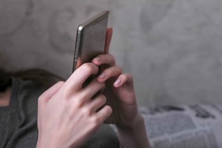 Woman lying on the couch and reading something at the mobile phone. Close-up hands with phone.の写真素材