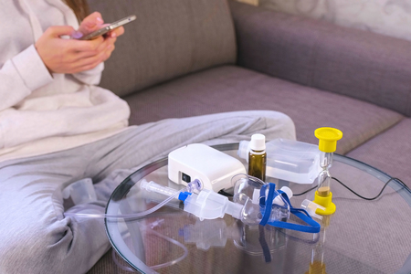 Preparation for inhalation. Nebulizer, mask and medicine on the glass table. Unrecognazable woman with mobile phone.の写真素材