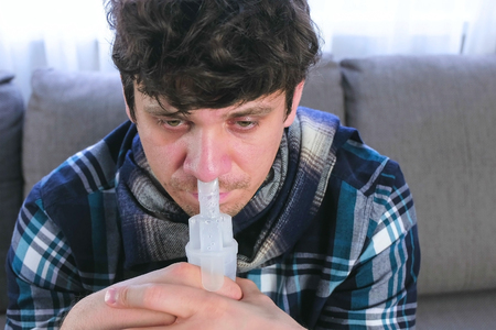 Sick man inhaling through inhaler nozzle for nose. Close-up face, front view. Use nebulizer and inhaler for the treatment.の写真素材