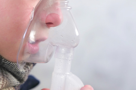 Sick boy inhaling through inhaler mask, nose and lips close-up side view. Use nebulizer and inhaler...