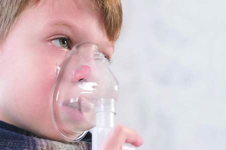 Sick boy inhaling through inhaler mask, face close-up side view. Use nebulizer and inhaler for the treatment.の写真素材