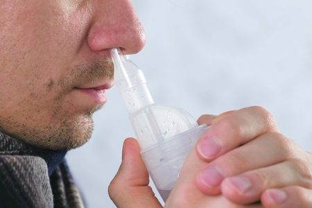 Sick man inhaling through inhaler nozzle for nose. Close-up nose, side view. Use nebulizer and inhaler for the treatment.の写真素材