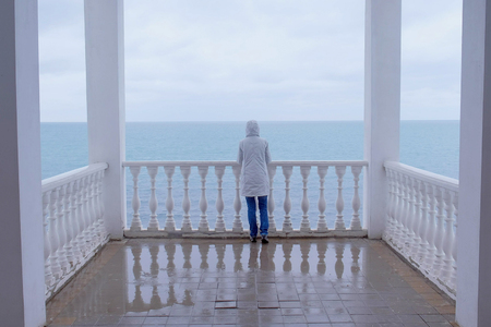 Woman in the white jacket admires at sea on beautiful terrace with sea view. Back view.の写真素材