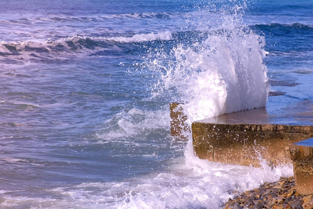 Splashes of water from the stormy waves breaking on the breakwater on waterfront. Side view.の写真素材