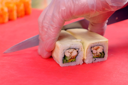 Chef cuts rolls with chicken, cucumber, tomatoes and cream cheese on top. Hands close-upの写真素材