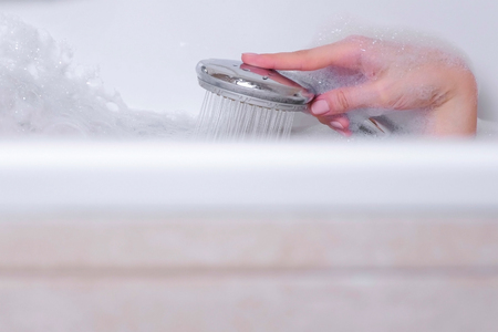 Woman is taking a bath with foam. She pours her body water from the shower. Hand close-upの写真素材