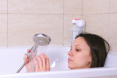 Woman is taking a bath. She pours her body water from the shower. Close-up face