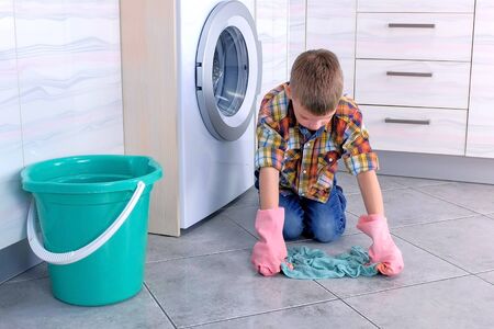 Boy in rubber gloves washes the floor in the kitchen. Childs home dutiesの写真素材