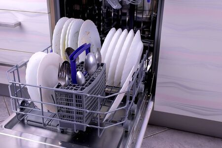Dishwasher basket with dirty white dishes and cutlery in the kitchen. Close-up view.の写真素材