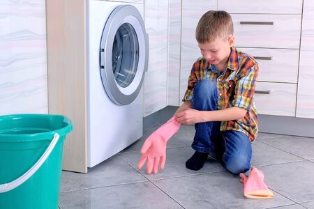 Boy puts on rubber gloves to clean the kitchen floorの写真素材