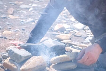 Dad and son are igniting the coals in the bonfire on the stones brazier with wooden sticks, hands...