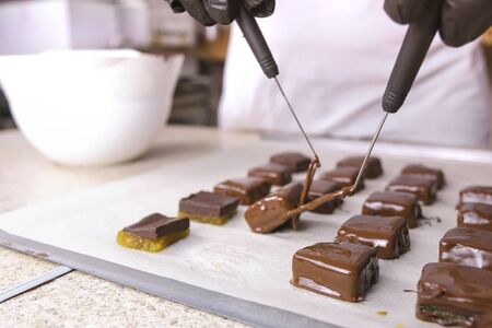 Production of chocolate candies. Hands close-up. Baker dips candies in melted chocolate and put it on baker paper to dry. Production of chocolate candies. Hands close-up.の写真素材