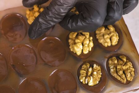 Bakers hands put the halves of walnuts on the chocolate candy in the formsの写真素材
